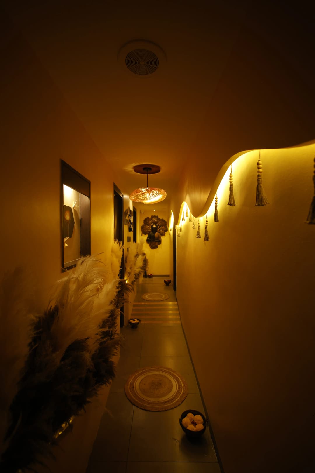 Hallway of verosha the boho spa, with ambient lights, design on the right and photos and photo frames on the left with buddha statue hanged on the wall straight